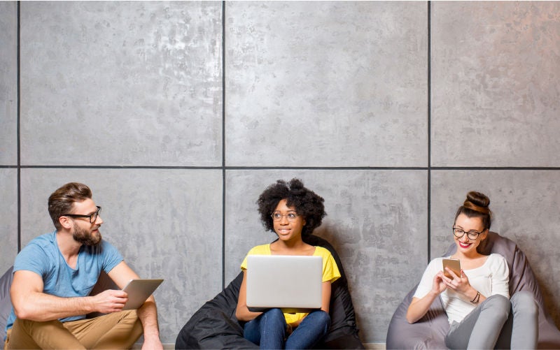man and two women sitting on loungers looking at their devices