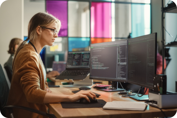 Woman at work desk viewing two monitor screens